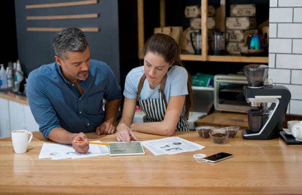Two colleagues reviewing records together over a tablet and printouts