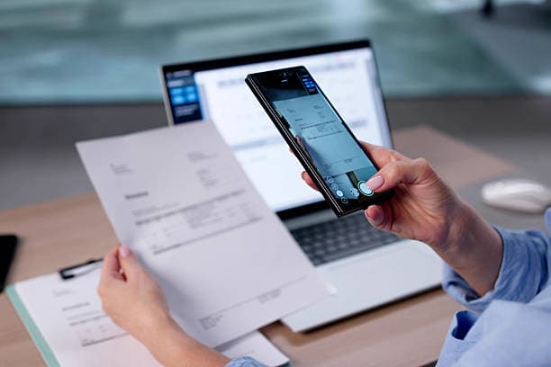 A client document being captured with a phone next to a laptop